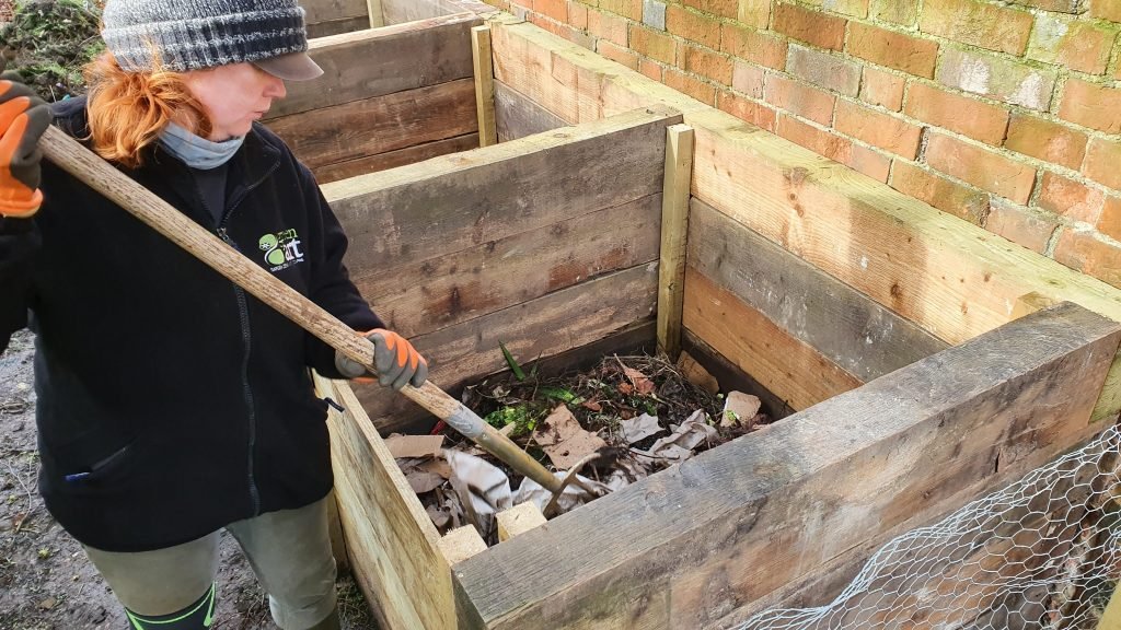 Photo of Jenny using a fork to turn the compost in a bin