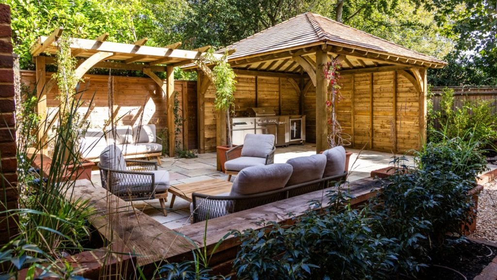 timber pergola housing a sophisticated BBQ in the background. Raised garden beds and pond with water feature surround an entertaining area.