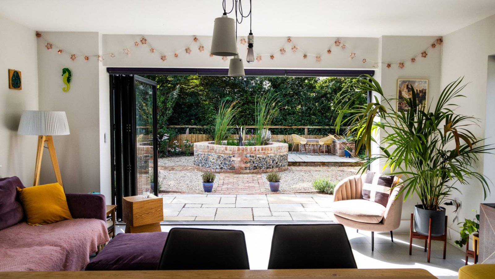 Open bifold doors of this new detached house open onto an Italian-inspired courtyard complete with feature brick and flint circular pond.
